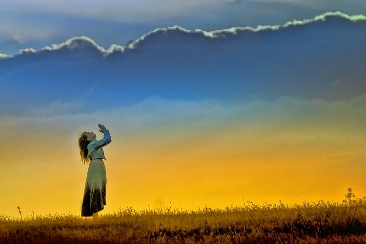 A woman holding her arms up in praise against a backdrop of a sunset sky