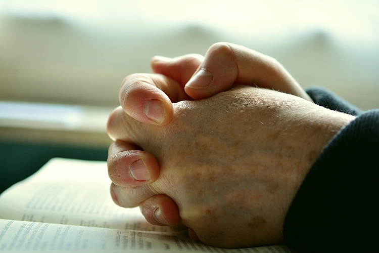 Hands clasped in prayer on top of a book