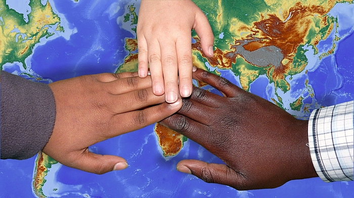 Three hands - one white, one brown, one black, touching on top of a map of the world