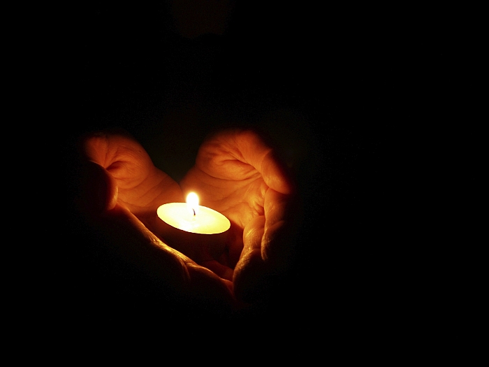 Hands held together in a heart shape holding a lit tealight candle