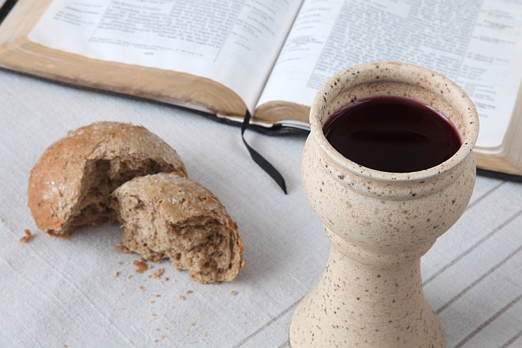 Chalice with red wine, bread and Holy Bible on a tablecloth. Shallow dof