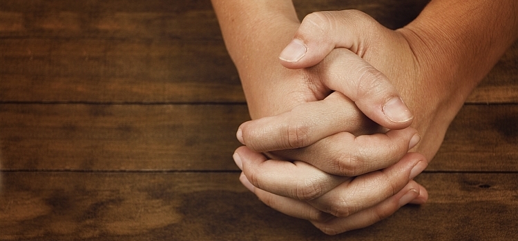 Hands clasped in prayer on a wooden table