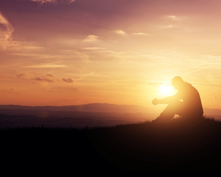 Man praying as the sun rises in the mountains.