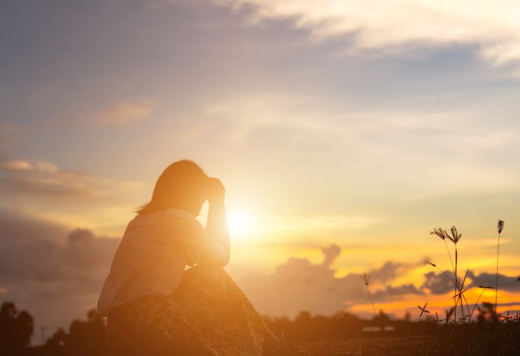 a woman sitting and prayer with a sunset sky in the background