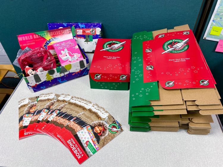 A table with flat-packed Operation Christmas Child shoeboxes, leaflets and a filled shoebox with an assortment of toys and gifts