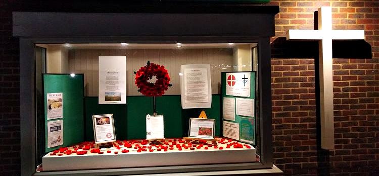 The end of the Christ Church building at night showing an illuminated white cross and a lit Remembrance Sunday window display with poppies and a poppy wreath