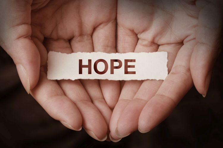 The word hope cut out on a piece of paper being held in someone's hands