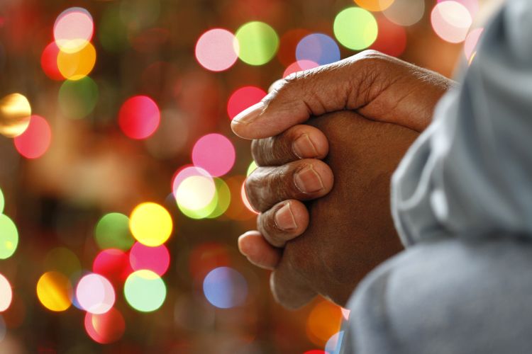 Hands clasped in prayer with colourful lights in the background