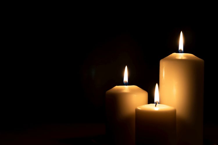 Three lit pillar candles - one small, one medium, one large, against a black background
