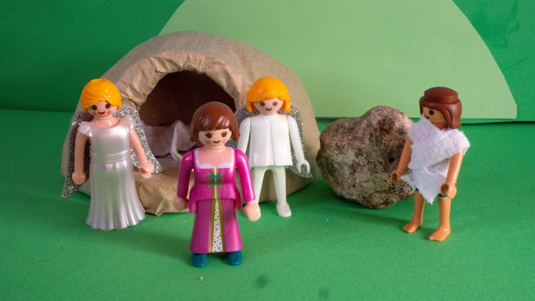 A Playmobil scene depicting Mary at the empty tomb with two angels behind her and Jesus standing next to her