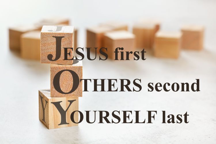 Three wooden cubes stacked on top of each other spelling 'JOY' with the words 'Jesus first, others second, yourself last"
