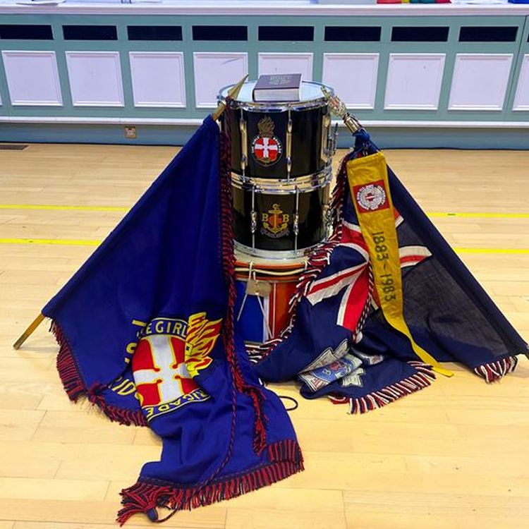 The Girls' Brigade colours and Boys' Brigade colours draped either side of three drums stacked on top of each other with a Bible on the top of the stack of drums