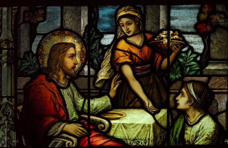 A stained glass window depicting Jesus with Martha standing next to him and Mary sitting at his feet