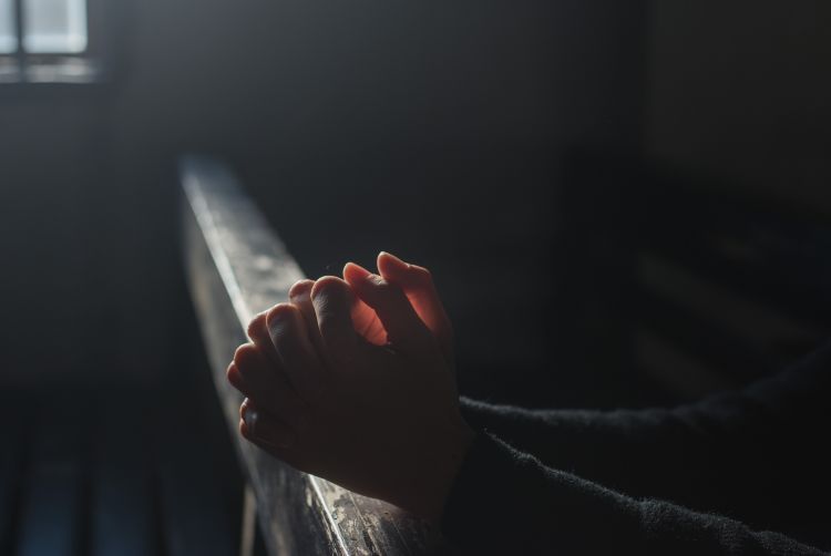 Hands clasped in prayer on a pew