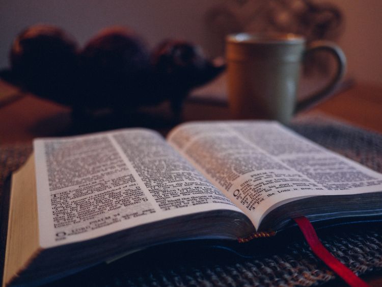 An open Bible on a table with a mug in the background