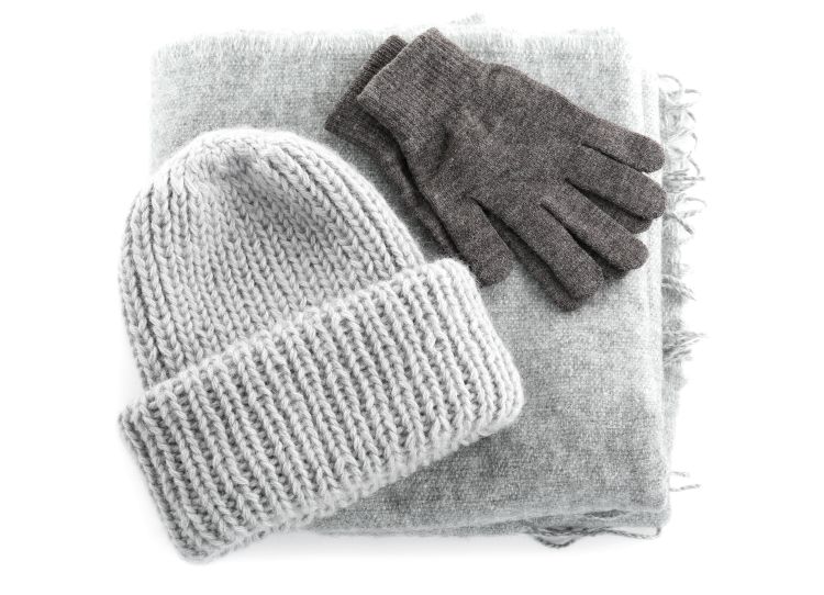 A grey woolly hat, grey gloves and a grey woollen scarf on a white background