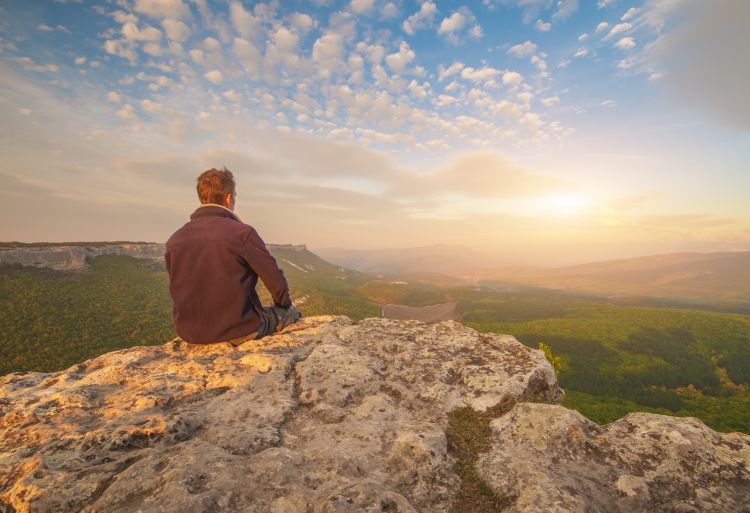 A man sitting on a mountain edge and looking to the sun.