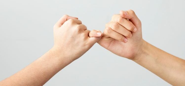 Two hands with little fingers interlinked, making a 'pinky promise'