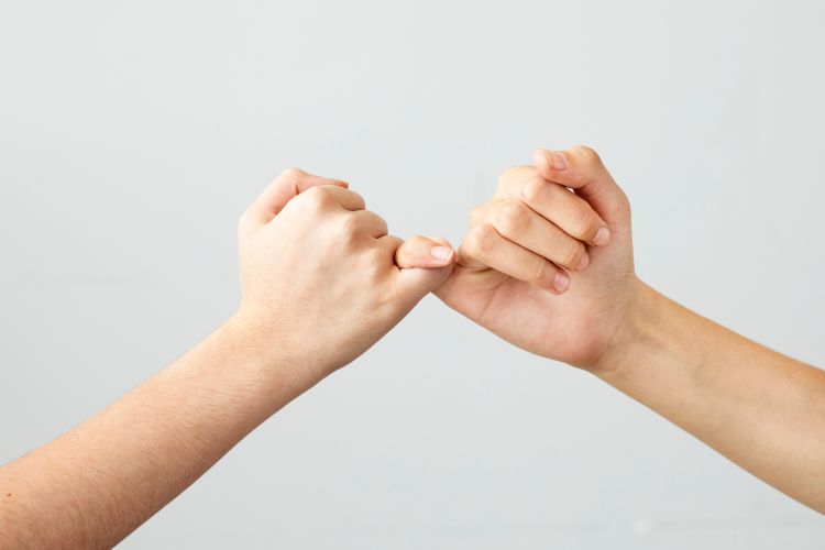 Two hands with little fingers interlinked, making a 'pinky promise'