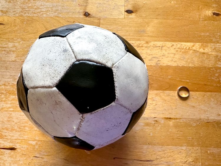 A football on a wooden surface next to a wedding ring