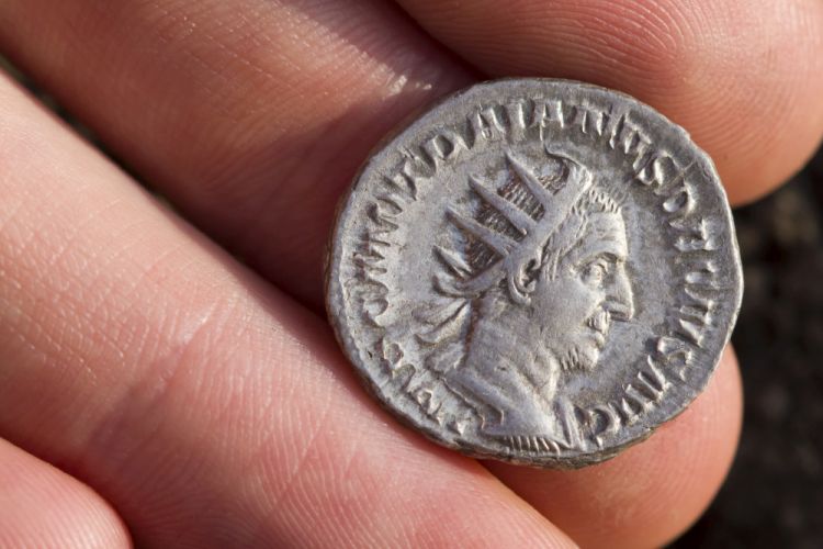 A hand holding a Roman silver coin with a portrait of Caesar