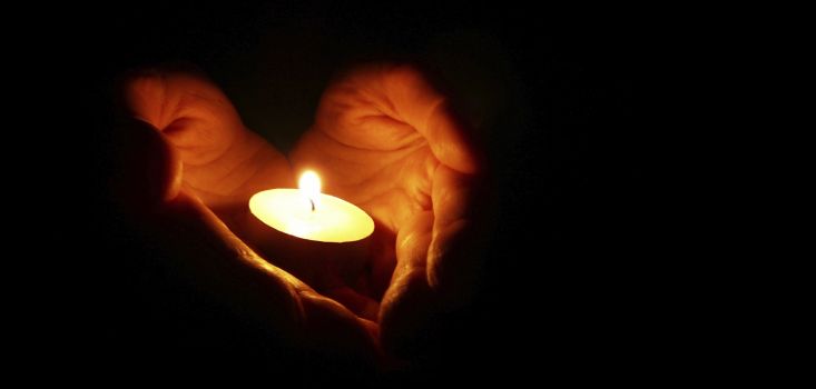 Hands held in a heart shape holding a lit tealight candle