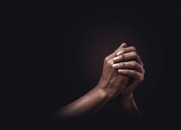 Hands clasped in prayer on a black background