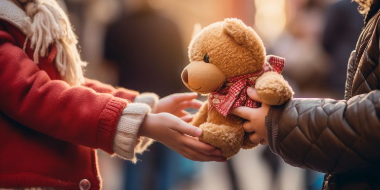 A child's hand receiving a teddy bear at a charity event