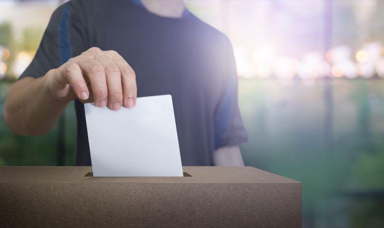 A hand holding a ballot paper inserting it into a ballot box