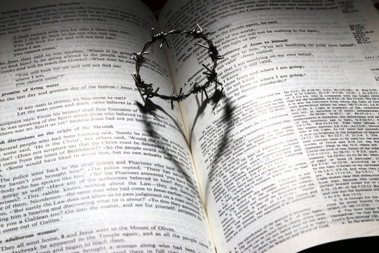 An open Bible with a miniature crown of thorns in the middle casting the shadow of a heart
